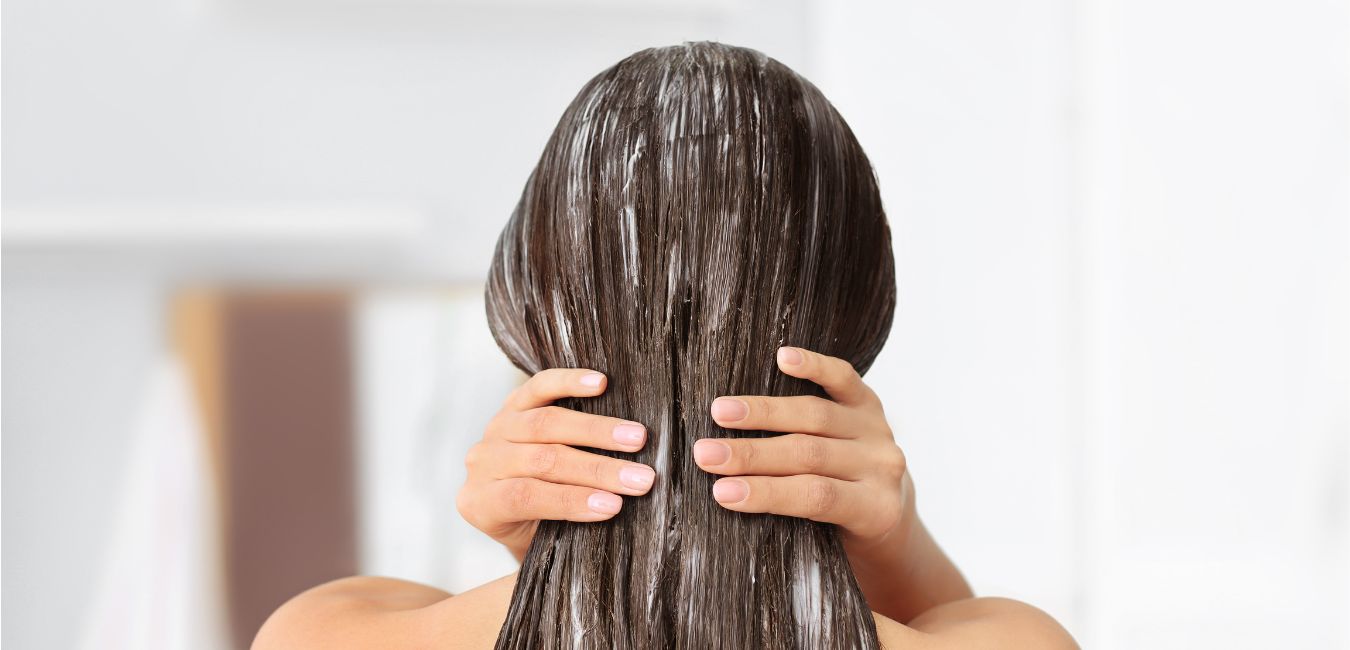 Se ve una mujer por detras que está aplicandose un producto en el cabello y está masajeandolo para que el cabello absorba mejor el producto.